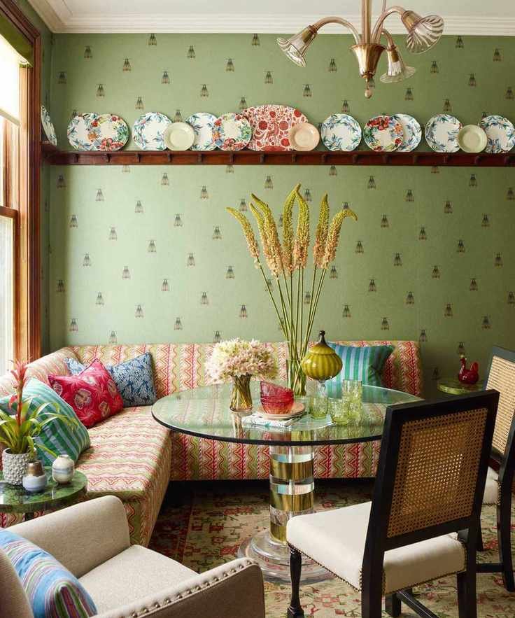 Green wallpapered dining nook with striped banquette seating, glass circular dining table and rattan backed cream chairs