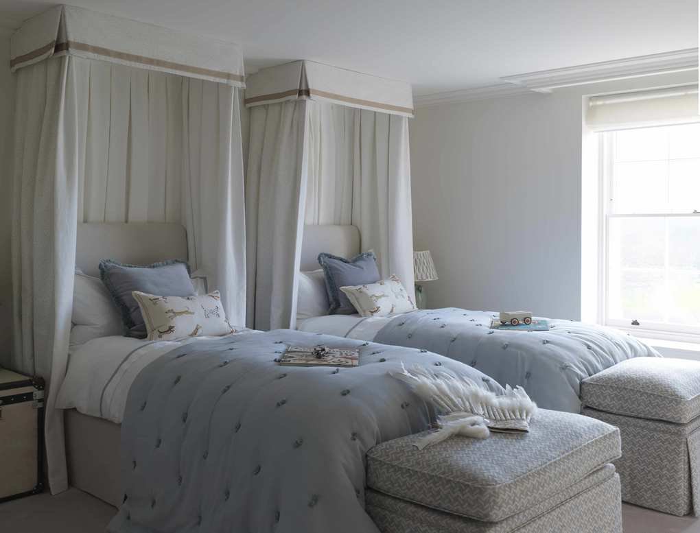 Twin beds with white canopies around headboards and storage space at the ends of the beds showing hotel-style shared bedroom ideas.