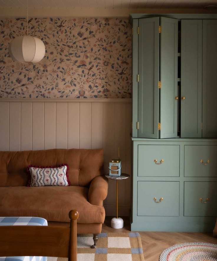 small snug area with paneled walls and half floral wallpaper, a tan sofa and a blue custom cabinet that folds out to reveal the TV