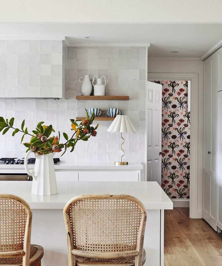 shot of white modern kitchen with white ceramic tiles and white countertop and cane bar stools and wooden floor