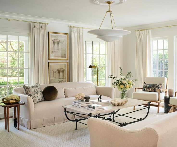 warm minimalist living room with all neutral decor, a wrought iron coffee table, arm chairs with foliage printed cushions and a skirted couch