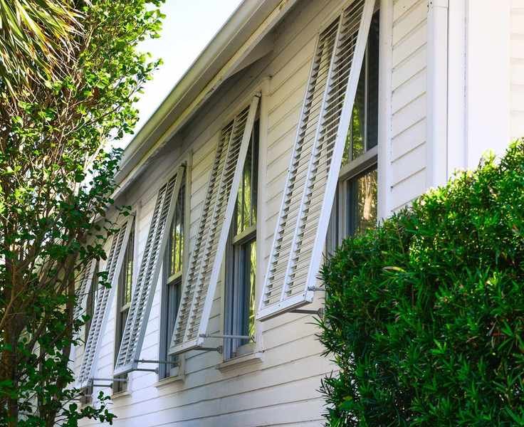 storm shutters on windows on a white sided house, propped open on a sunny day.