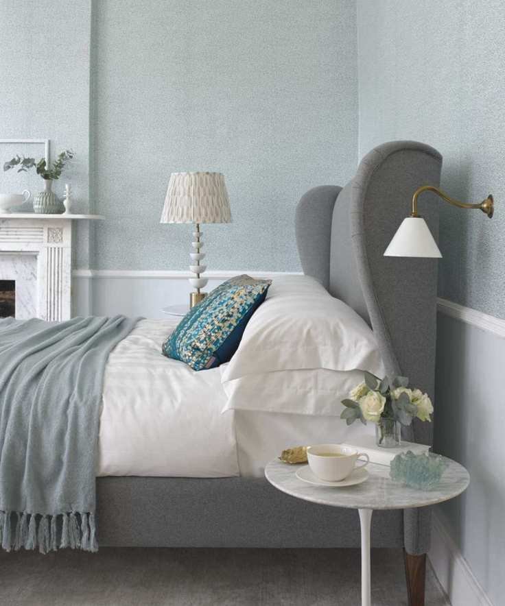 Neutral bedroom with grey bed and white bedding, white sconce and marble bedside table