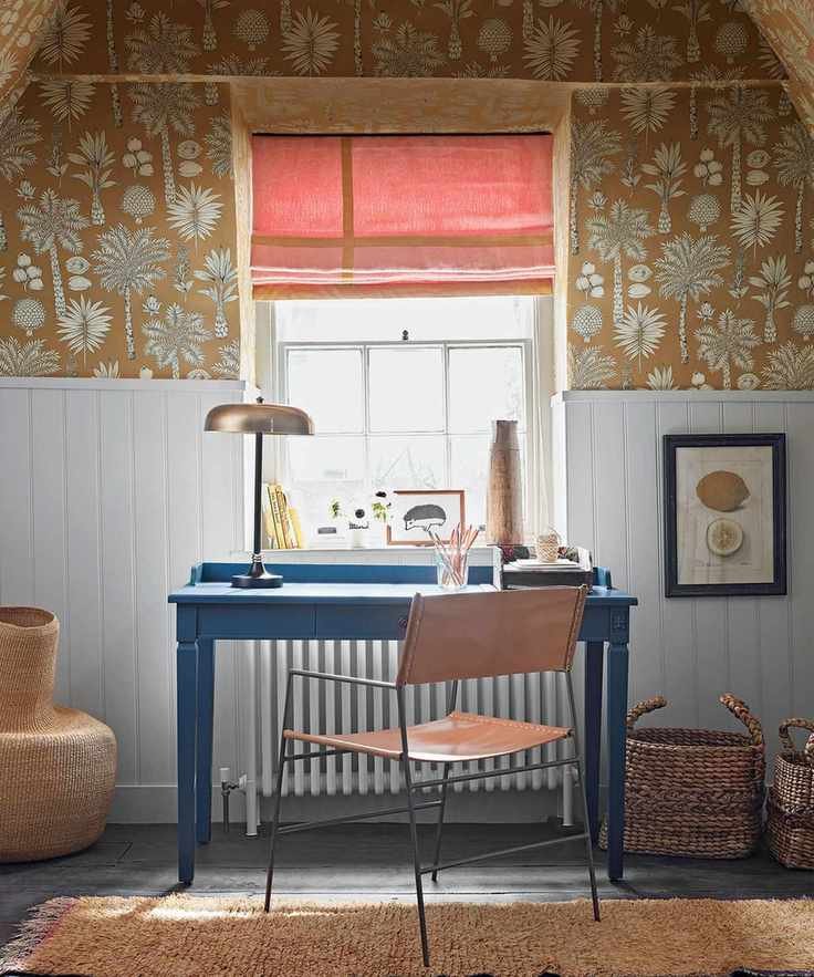 Workspace featuring a blue desk, leather chair, ochre floral wallpaper, light blue paneling, and woven baskets