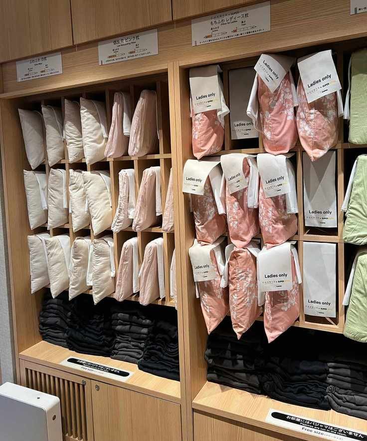A wooden shelving unit filled with different pillows in different colored pillowcases.