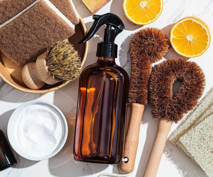 An amber glass bottle surrounded by lemons, baking soda and scrubbing brushes