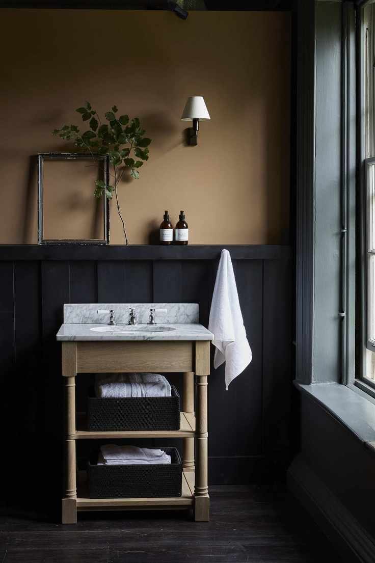 yellow ochre bathroom with marble topped vanity, black panelling, wall light, green painted window, dark wooden floors