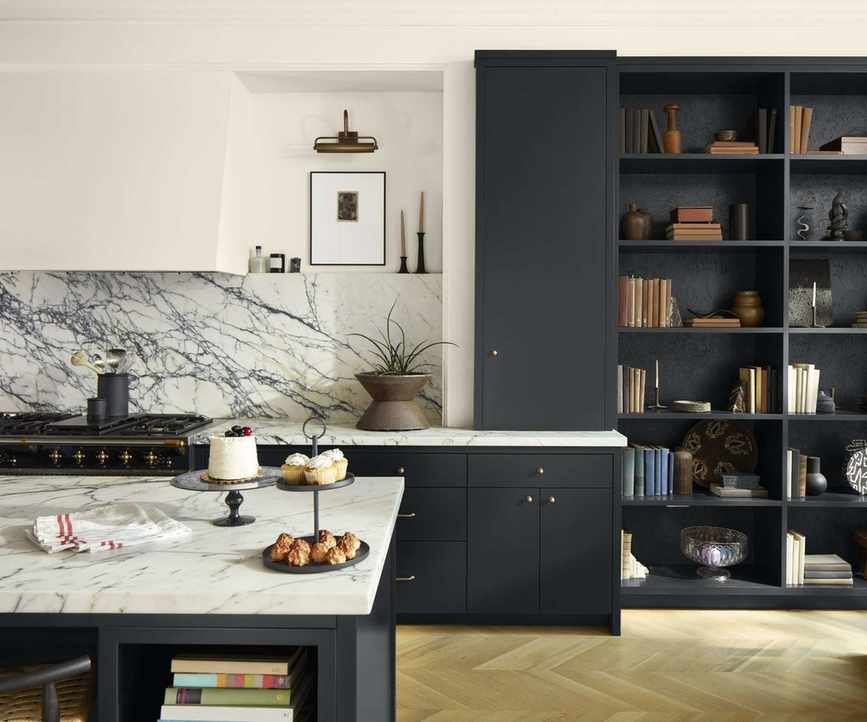 A kitchen with black cabinets, white walls, and a marble countertop and backsplash