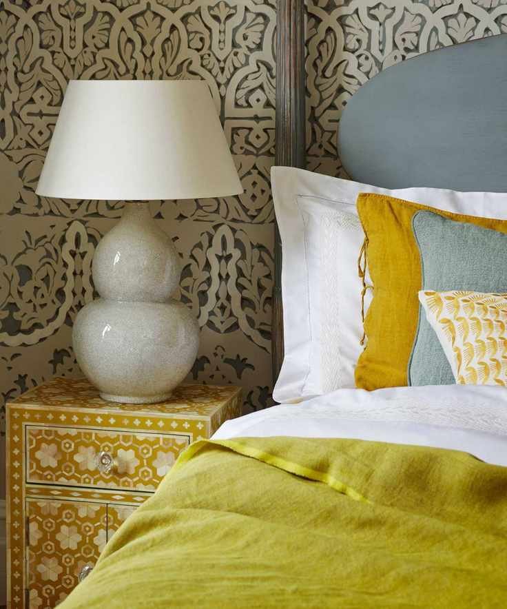 A bedroom with patterned wallpaper and a bed with light blue headboard and white bedding