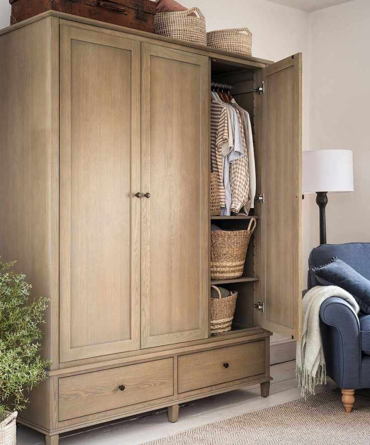 A large three-door wooden closet, with one door open showing some hanging shirts and two woven baskets.
