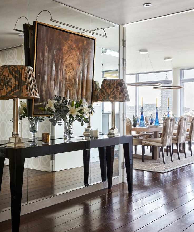 A hallway with lamps on a console table and a mirrored wall