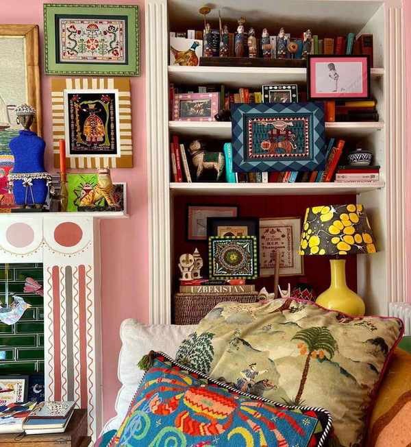 A pink sitting room with shelving, on the shelving are lots of books, trinkets and decorative items including frames which have been handpainted