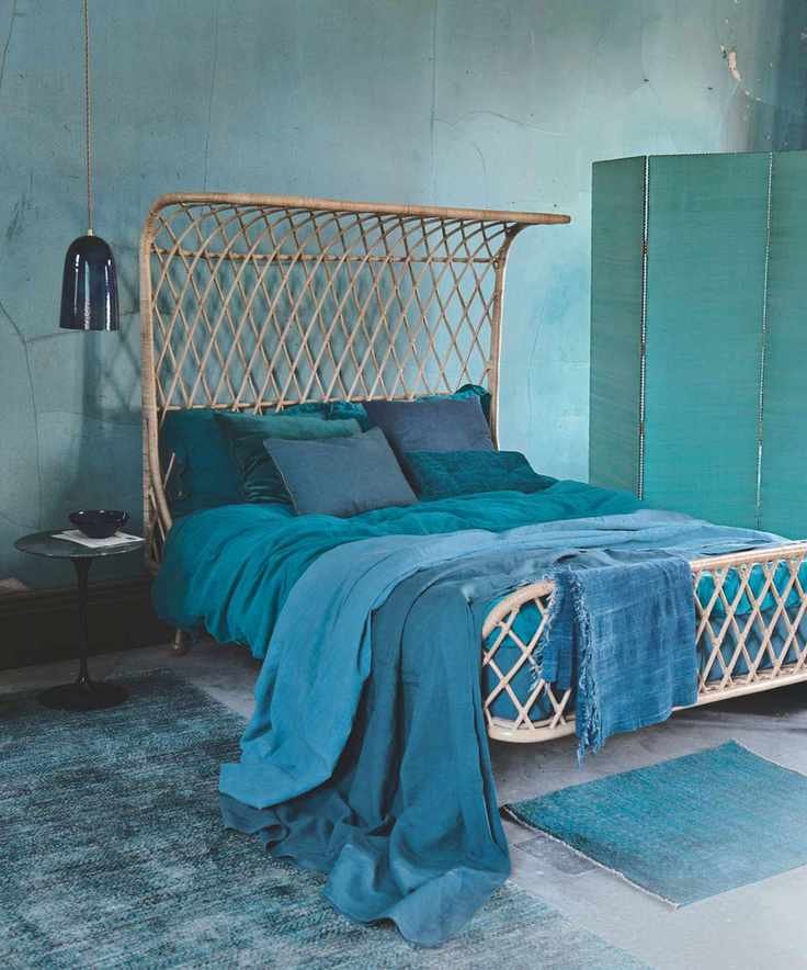 A blue bedroom with blue walls, rattan bed, blue blankets, a blue screen and two blue rugs.