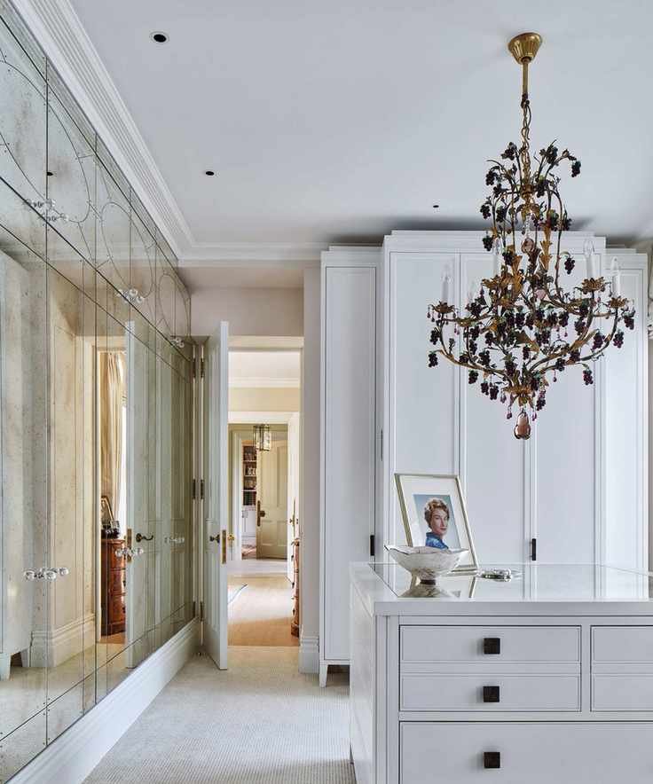 A chic white dressing room with a mirrored wall and a gold and black chandelier