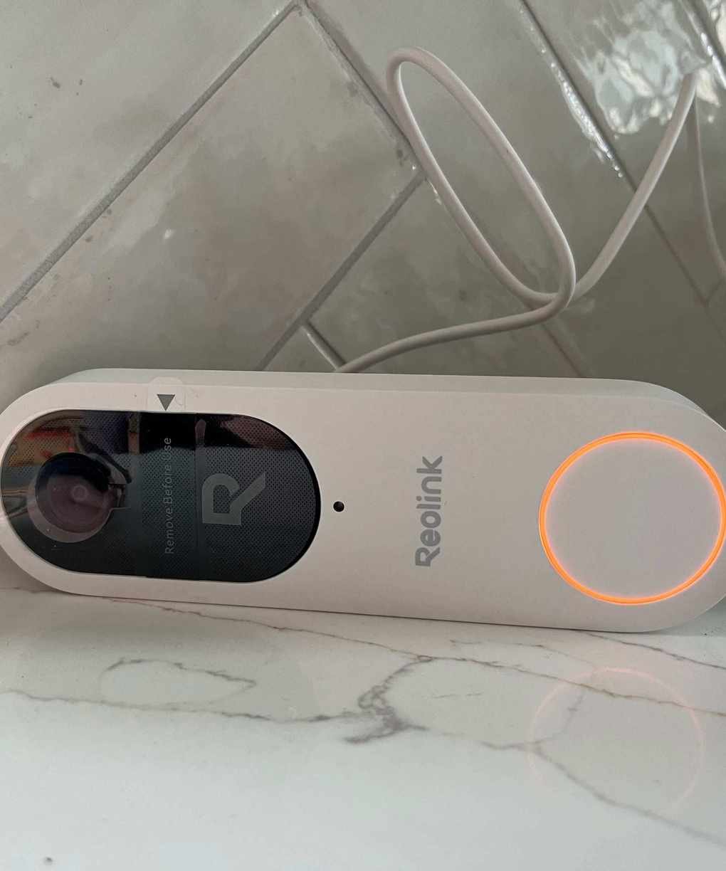 Reolink video doorbell (battery) plugged in and charging, displaying orange charger light.