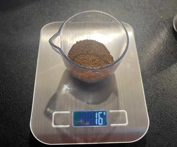 Fine ground coffee beans in a clear plastic container on digital weight scales.