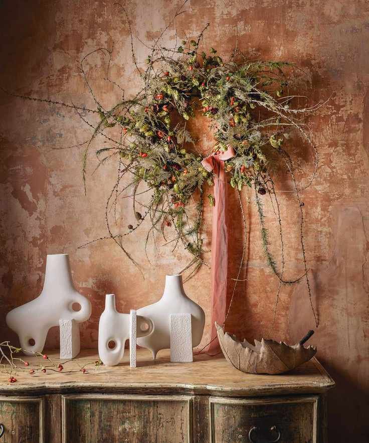 Sideboard with modern vases below a green and red wreath with a red ribbon hanging on the wall above.