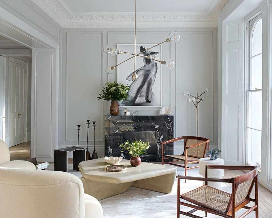 A classic white living room with cane and wood chairs, architectural light feature, stone coffee table and white cornicing.