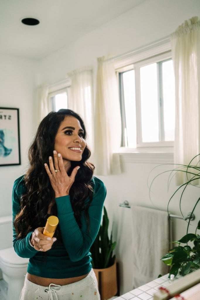 Brunette woman applying skincare in bathroom.