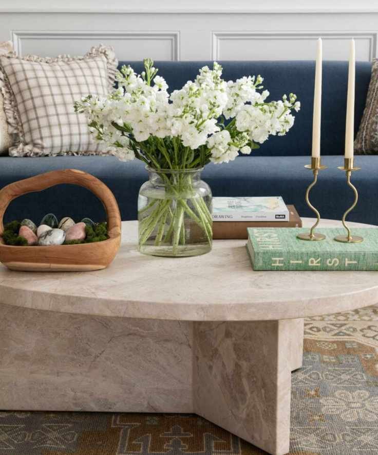 Living room with a navy blue couch and a marble round coffee table decorated for Easter with flowers and a wooden basket filled with decorative Easter eggs