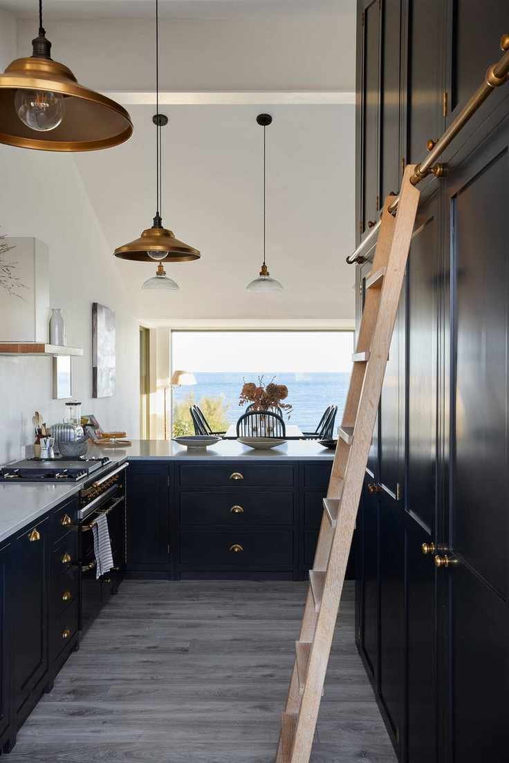 navy kitchen with cabinets up to ceiling with ladder, view to sea, copper pendant lights, galley style, white countertops, artwork, gray floor