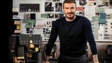 David Beckham stands in front of a large vision board, beside a black and gold coffee maker.