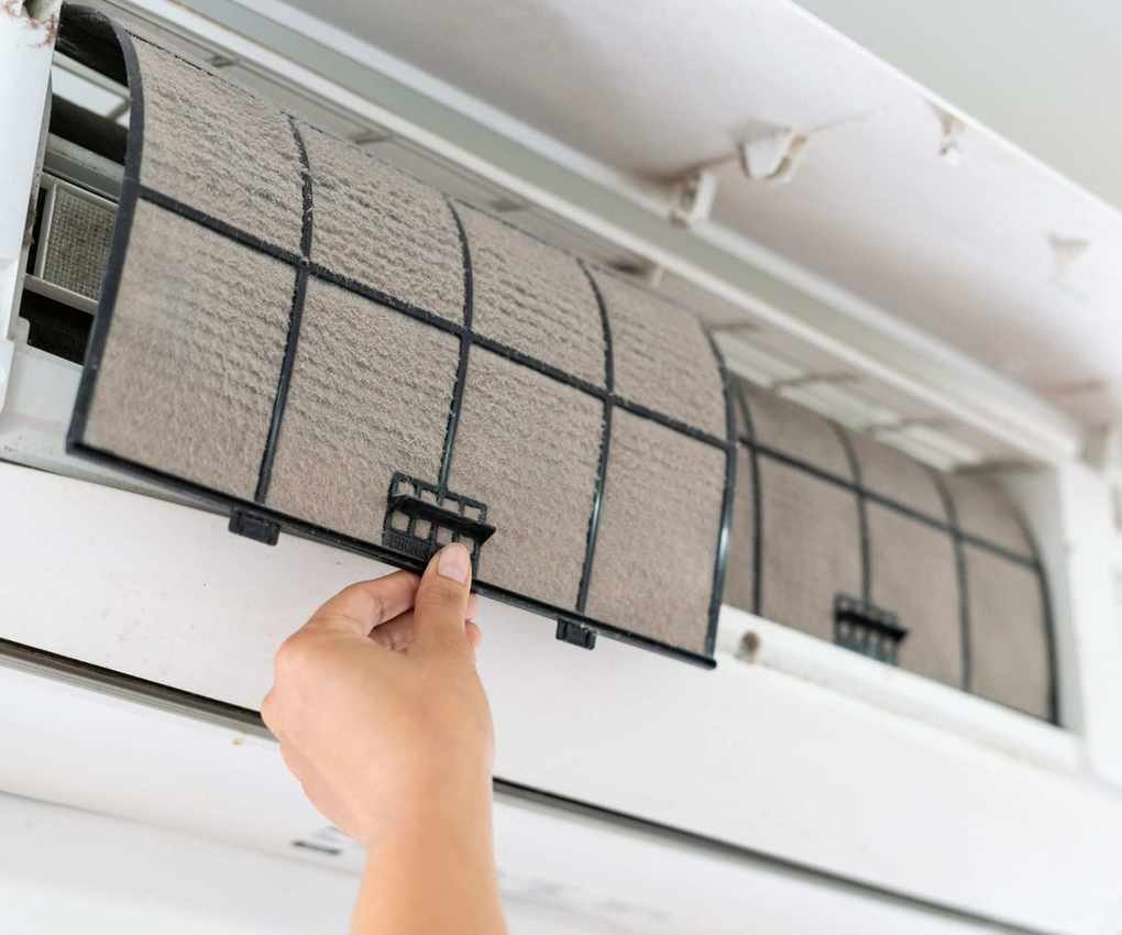 AC filter being pulled down from a wall mounted unit. It is covered in dust