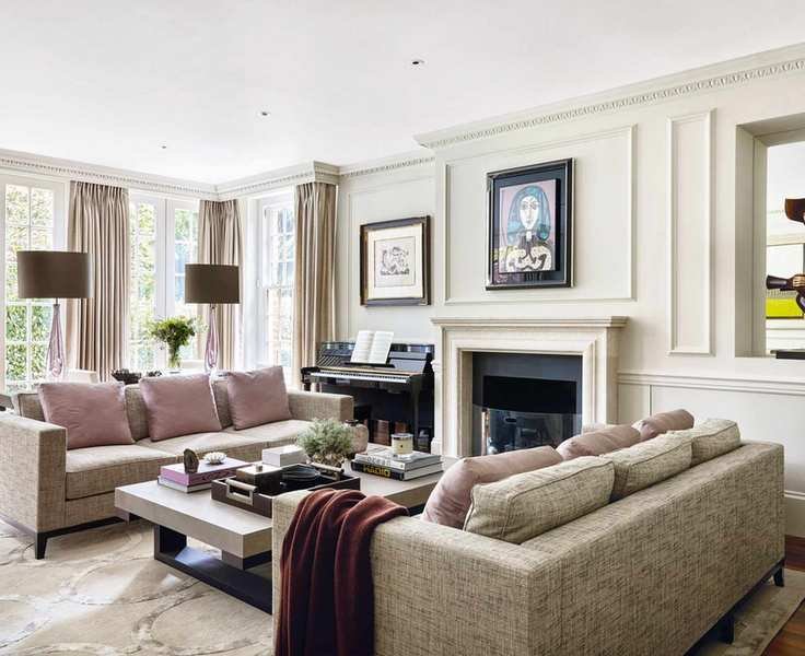 Bright living room with off white painted walls and paneling, spacious seating area with two gray three seater sofas, purple cushions, dark wood flooring with cream rug, twin gray table lamps, fireplace and piano