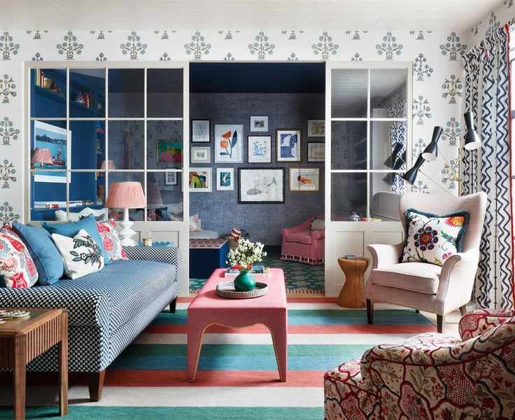 A broken plan living room with a colorful mixture of patterns in the choice of rugs, wallpaper, drapes and sofa fabrics.