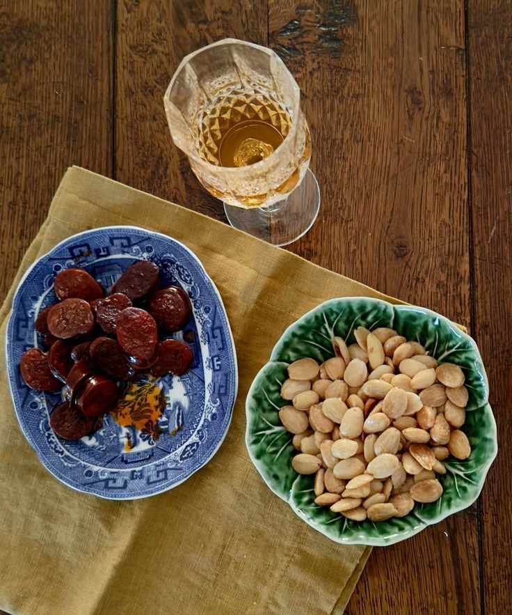 Bowl of sliced chorizo, nuts and a glass of sherry on a wooden table with a napkin