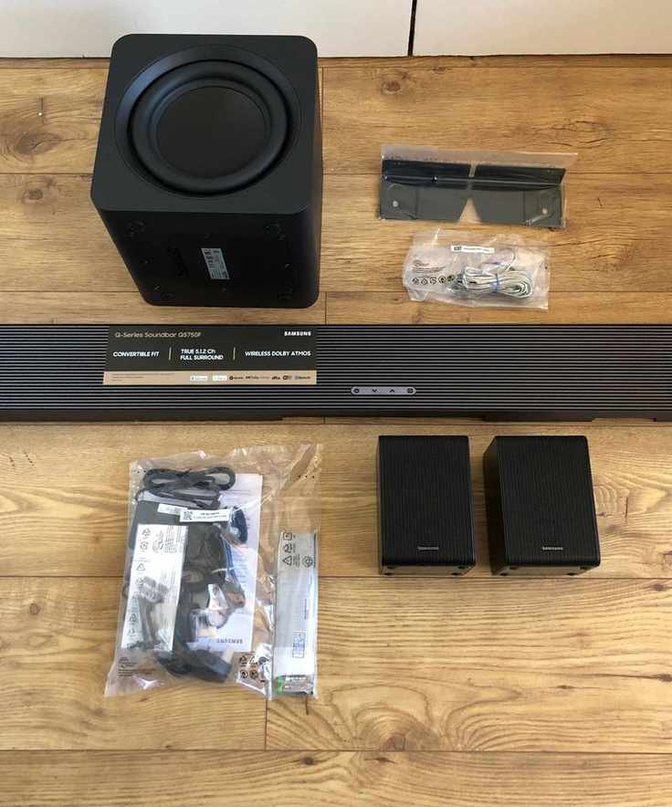 All components of the Samsung HW-QS750F soundbar on wooden floor.