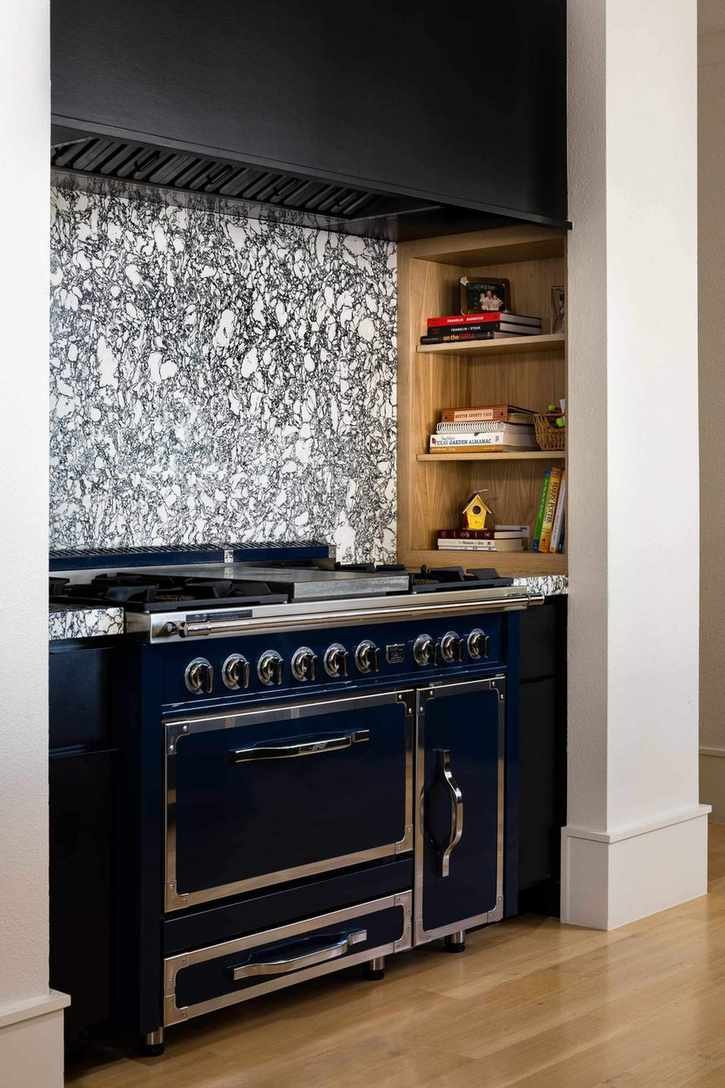Stove with veined stone backsplash and niche with cookbooks