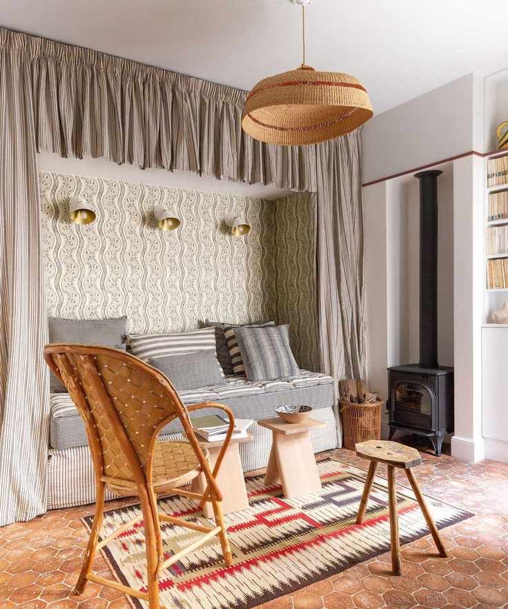 Bedroom with tiled floor, built-in bed niche with curtains and wallpaper, rattan armchair and wood side table and pendant light