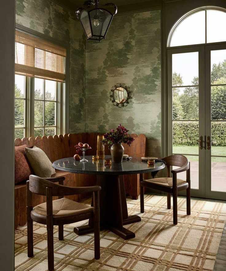 a dining nook with green wallpaper, a striped brown rug, a circular table, two chairs, and a built-in bench