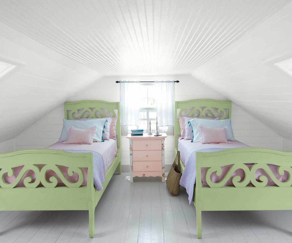 A white attic bedroom with light green single beds and a light pink side table between them.