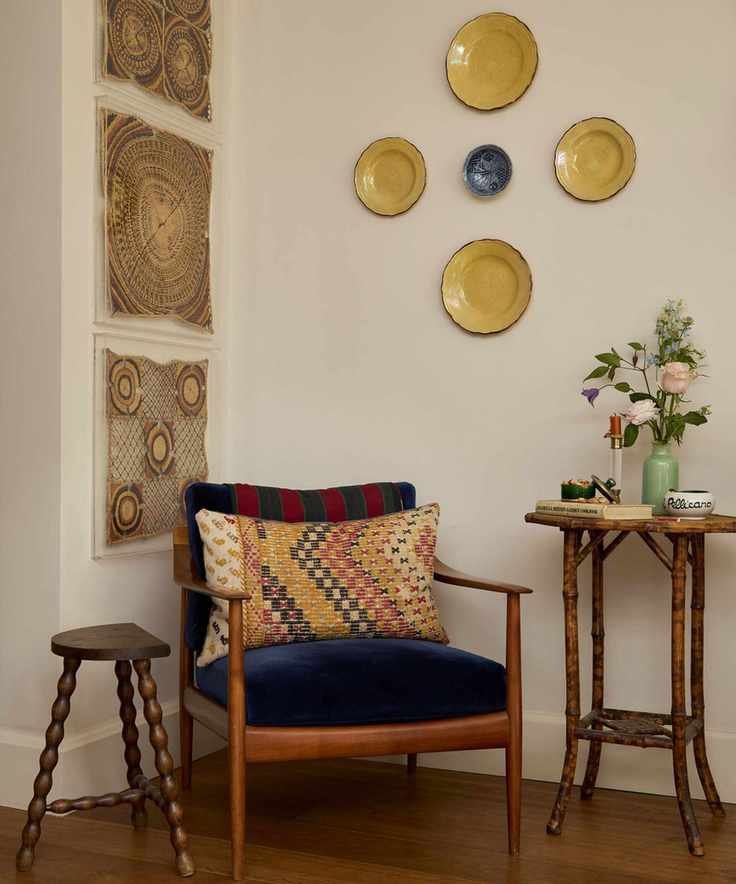 Eclectic hallway with vintage ceramic plates on wall, wood armchair and side table with antique wall hangings