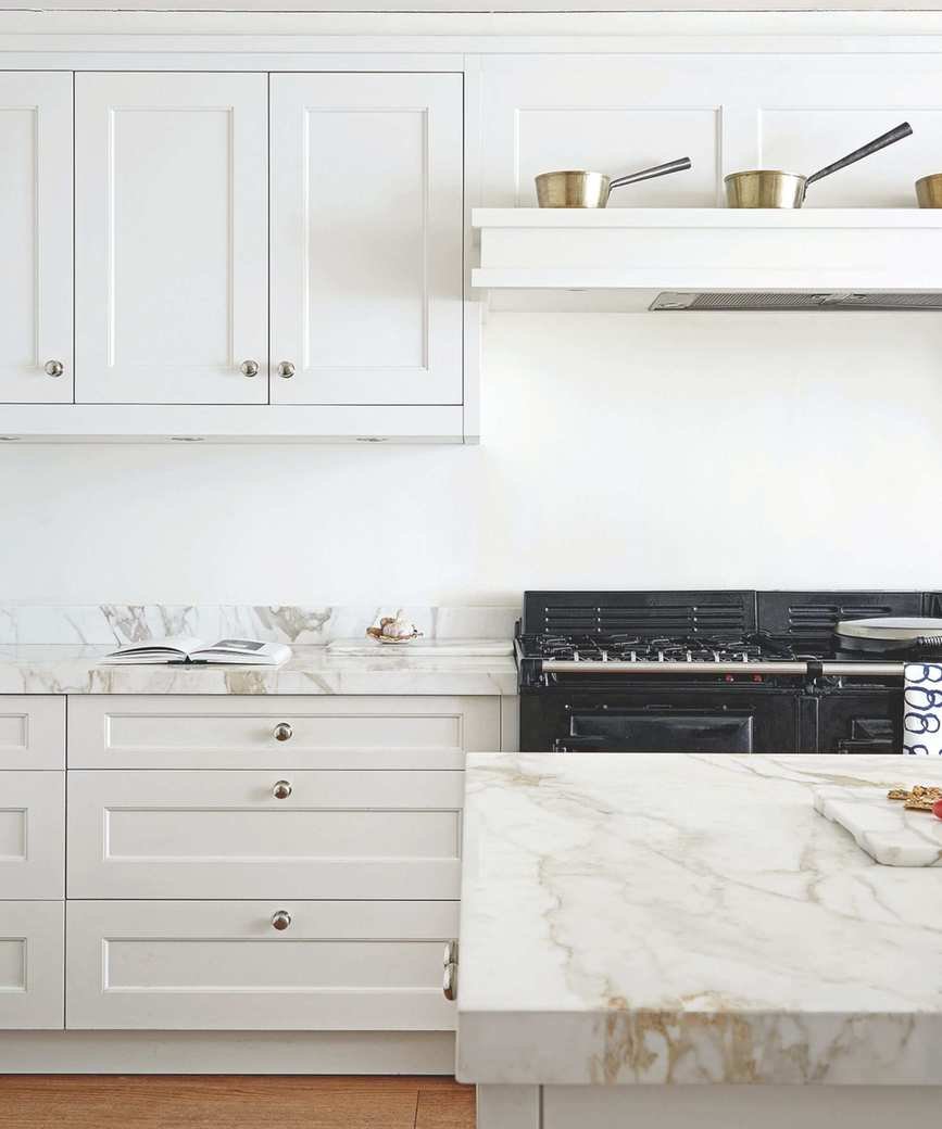 Bright kitchen featuring marble countertops and white cabinets with a large black oven and an open recipe book.
