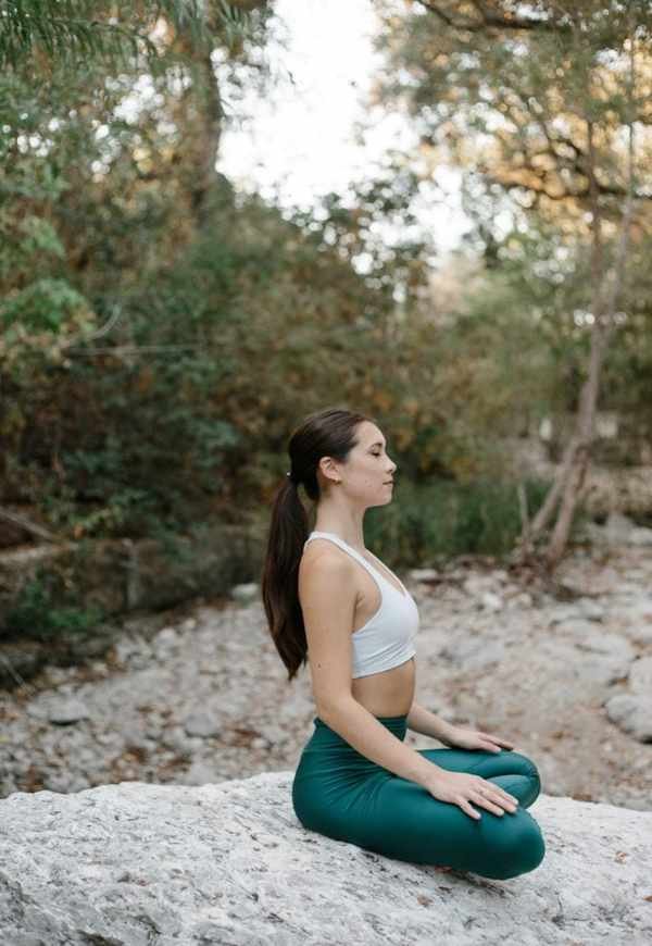 Woman meditating on rock outside.