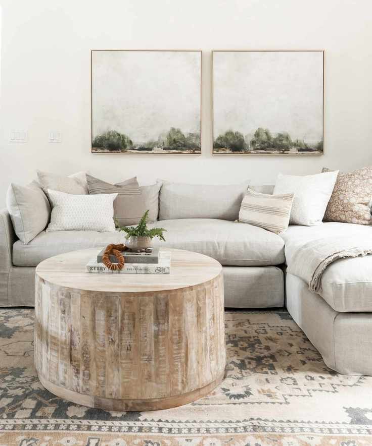 A white living room with pale grey sofa, tree trunk coffee table and landscape paintings