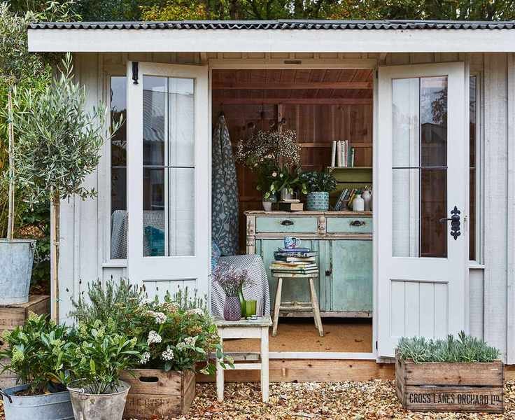 A pale gray shed demonstrating storage ideas for sheds, with vintage painted furniture and potted plants in front.