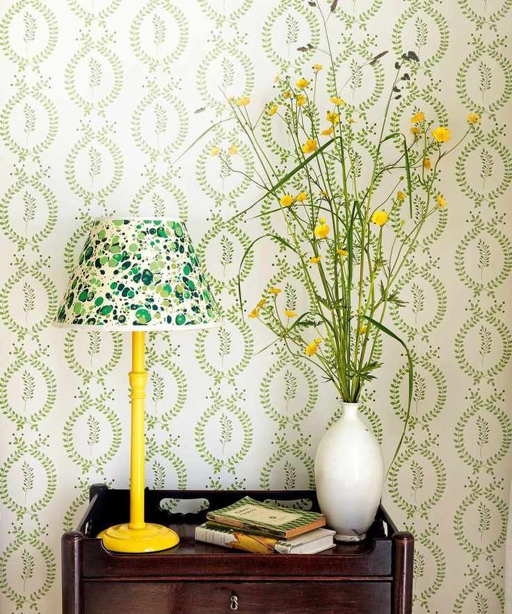 Table against green and white wallpaper with decorative lamp and vase