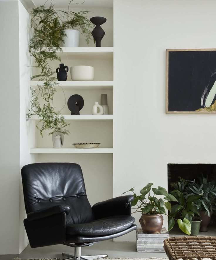 corner of living room with white walls with shelving, black leather swivel chair, lots of plants