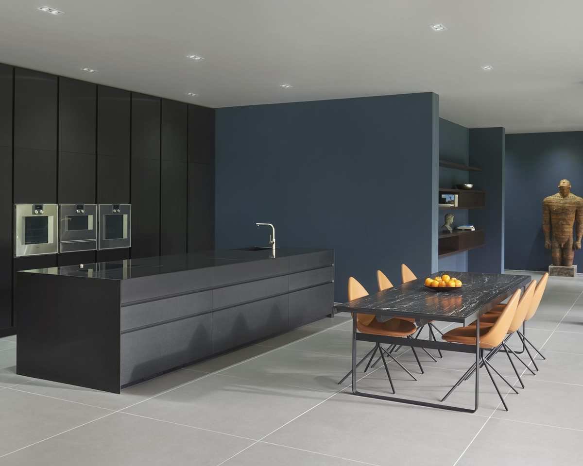 A black kitchen idea with black cabinets, blue walls, and orange dining chairs