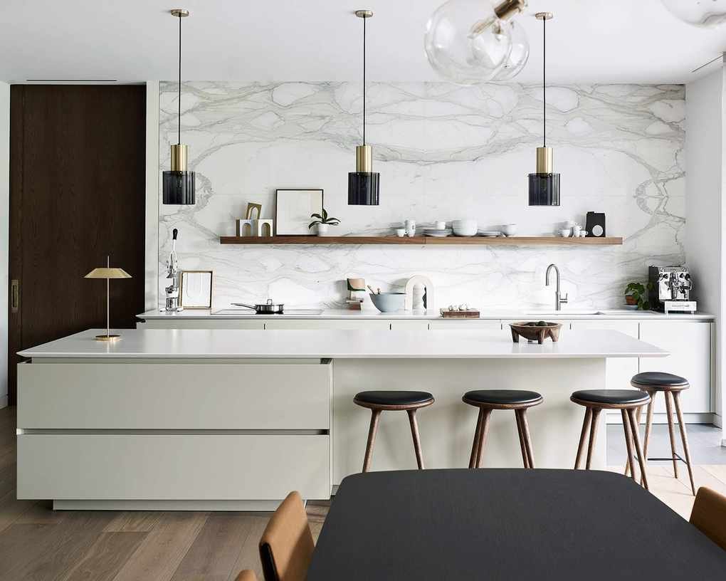 Chic white kitchen with an island featuring handleless drawers and a large marble backsplash