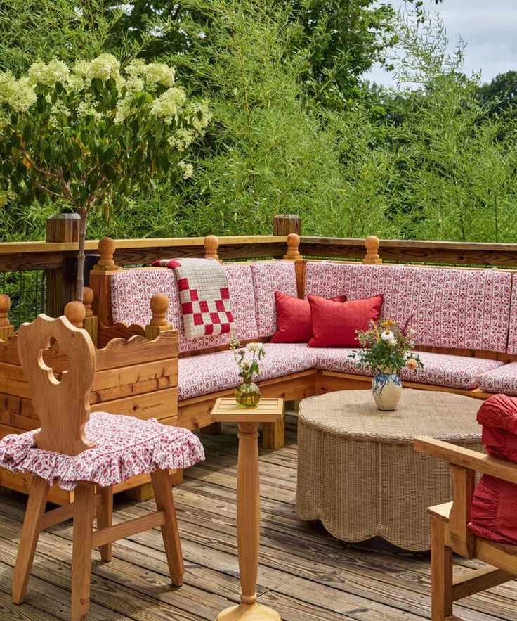 large wooden balcony patio with pine corner sofa styled with red and white patterned cushions, a patchwork throw and red cushions with a rattan scalloped coffee table and vintage pine dining chair