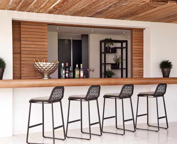 A garden bar showcasing a long wooden counter with black stools in a white outdoor setting.