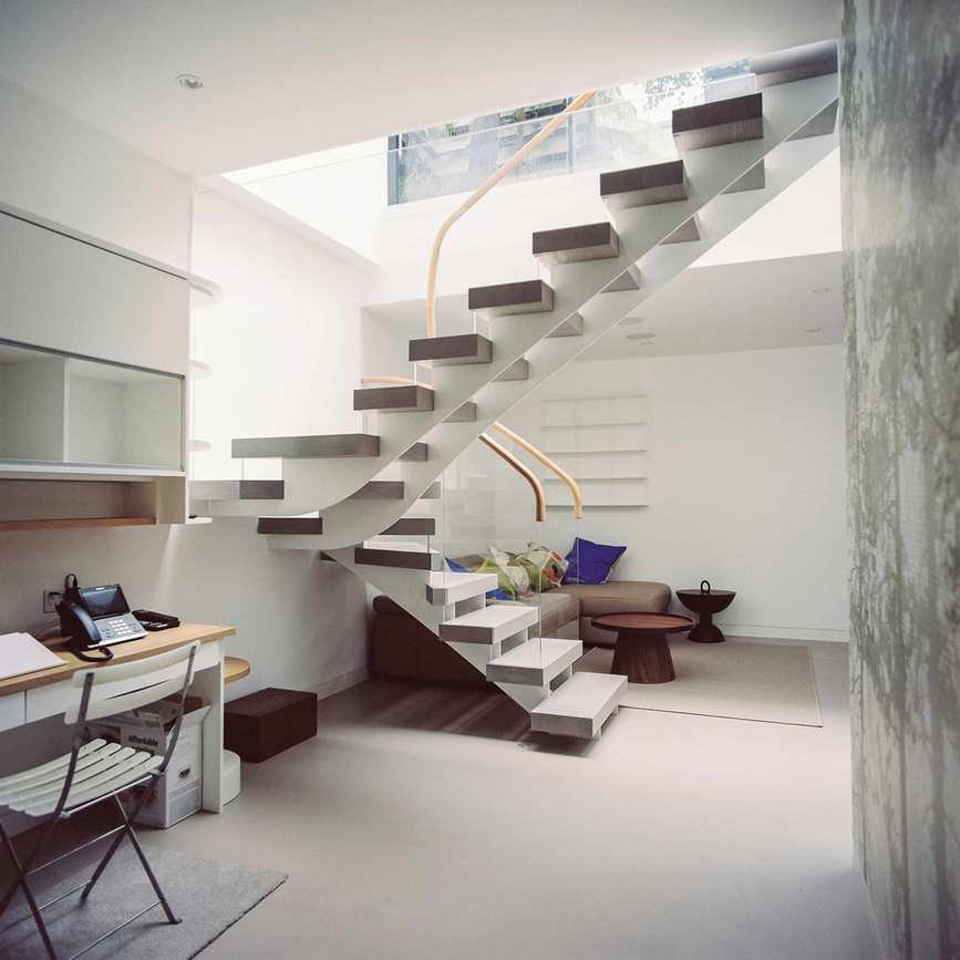 Open tread staircase with glass balustrade leading to basement with neutral decor with seating area and desk
