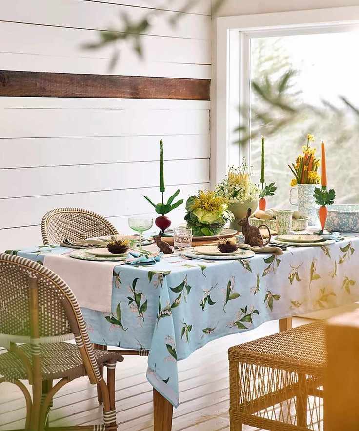 Spring table styled by Terrain with a blue floral tablecloth, wicker chairs, spatterware crockery and Easter decor with a bunny jug and carrot candle holders