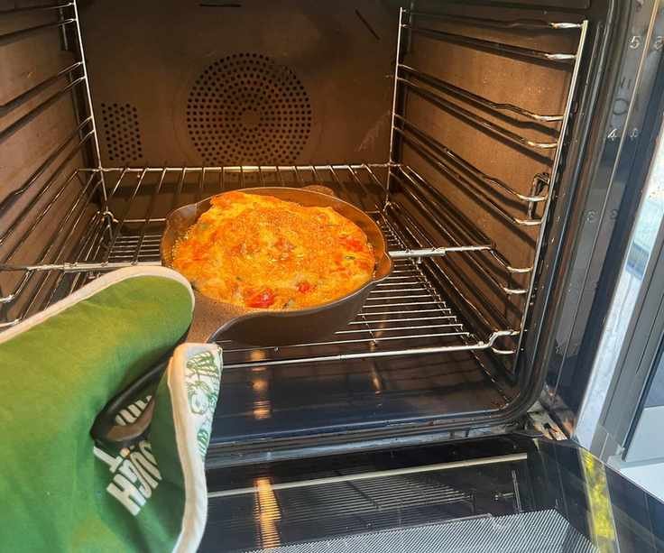 Lancaster Cast Iron Skillet being put into an oven with a frittata inside, being held with a green oven glove.