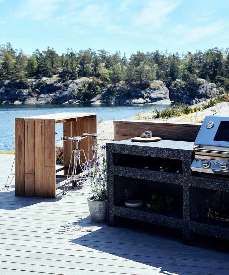 A garden bar with a BBQ and wooden bar overlooking a serene lake.